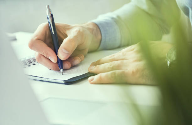 istock Businessman hand writing note on a notebook. Business man working at office desk. Close up of empty notebook on a blackboard with office supplies. 1153253015