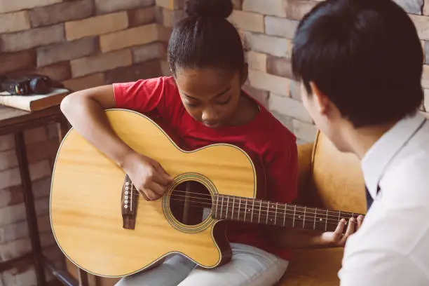 Photo of Male tutor teaching black girl to play guitar