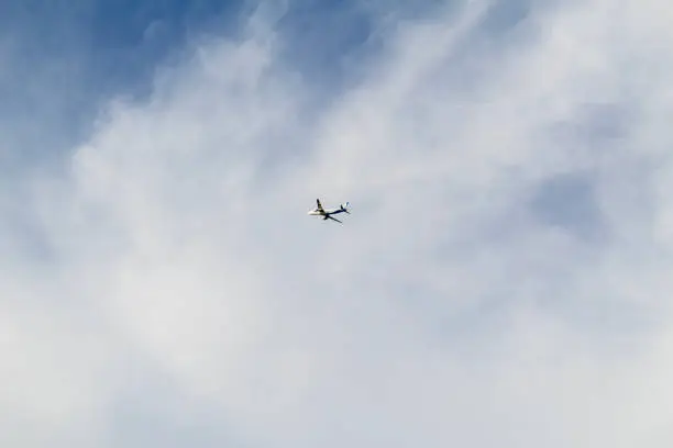 Photo of ground view of an airplane against thick clouds and blue sky looking up view