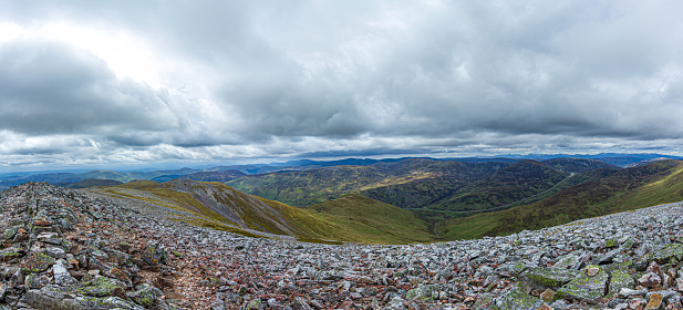 An panorama view of a Scottish mountain valley with a road and mountain range under a stormy huge white clouds sky