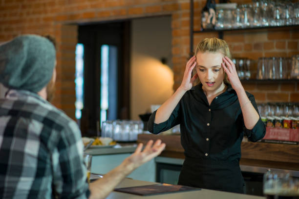 Stressed Out Waitress Stressed female young adult waitress holding her head in stress as customers complain to her behind the bar of a restaurant. She is wearing a black button up. stressed waiter stock pictures, royalty-free photos & images