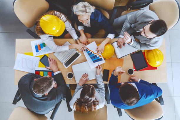 vista superior del grupo de arquitectos centrados dedicados en el uso formal que trabaja en el proyecto grande. en el escritorio son portátil, tableta, papeleo, tablas y café. - built structure coffee blueprint engineering fotografías e imágenes de stock