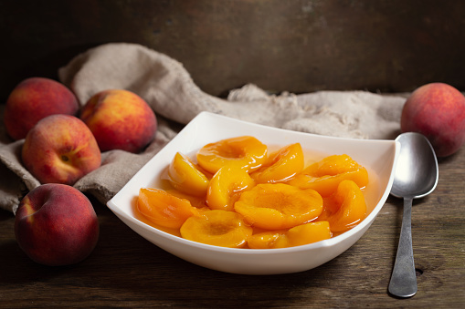 bowl of canned peaches with fresh fruits on wooden table