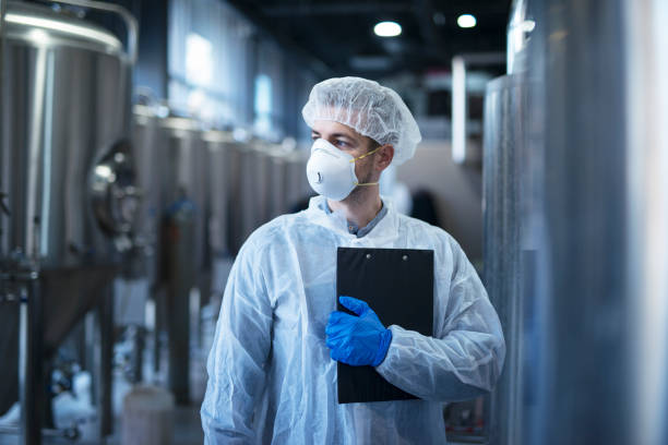 Technologist in protective white suit with hairnet and mask standing in food factory. Technologist at work. pharmaceutical industry stock pictures, royalty-free photos & images