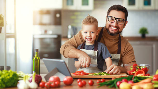 szczęśliwy ojciec rodziny z synem przygotowuje sałatkę warzywną - domestic kitchen people fun lifestyles zdjęcia i obrazy z banku zdjęć