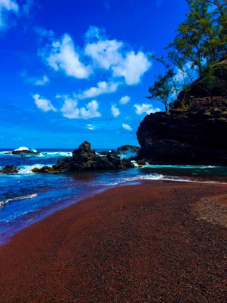 Red, sand beach whit a cloudy blu e sky and some trees in the background Red sandy beach with blue sea, blue sky and a few clouds hana coast stock pictures, royalty-free photos & images
