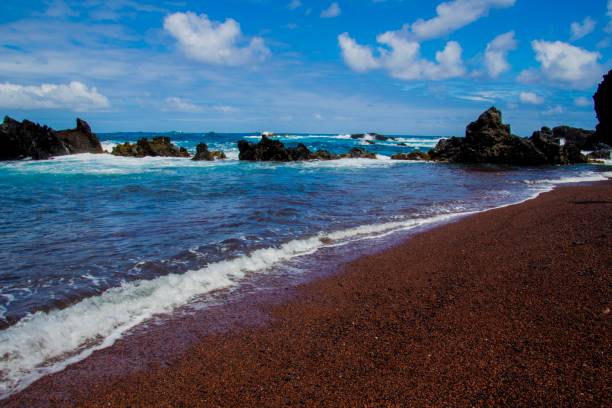 Red, sand beach whit a cloudy blu e sky and some stones  in the background