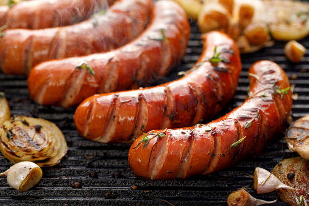 grilling sausages with the addition of herbs and vegetables on the grill plate, close-up. - sausage bratwurst barbecue grill barbecue imagens e fotografias de stock