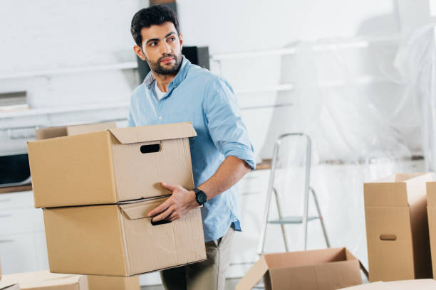 handsome latin man holding boxes while moving in new home stock photo