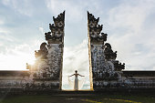 Welcome in Bali. Travel concept. Woman enjoying sunset on Balinese famous symbol - traditional gate in temple with beautiful view.
