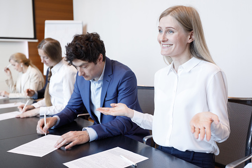Smiling confused female worker shrugs shoulders at business meeting