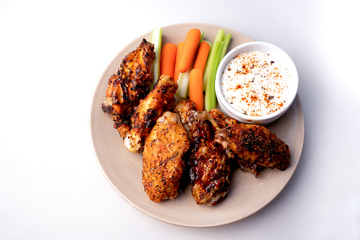 Plated Grilled, baked chicken wings with a side of blue cheese dip, celery and carrot sticks