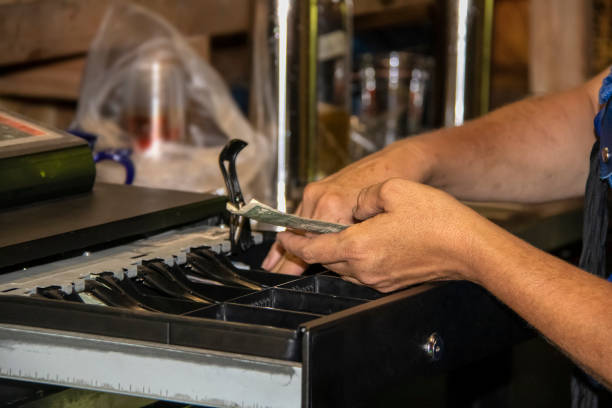 primer plano cosecha de mujer haciendo cambio en la vieja caja registradora con dinero americano en la mano con el fondo borroso bokeh del interior de antiguo edificio rústico - enfoque superficial - retail occupation cash register retail selling fotografías e imágenes de stock