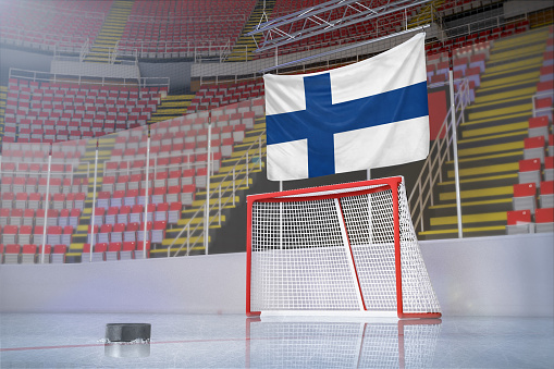 A hockey puck is on the ice rink in front of the goal and the flag of Finland