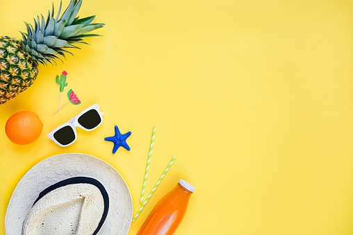 Summer vacation accessories. Straw hat, white sunglasses, earphones and flip-flops over yellow background. Copy space, flat lay.