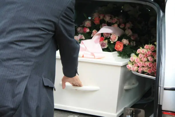 A funeral home employee takes out a white coffin of a hearse