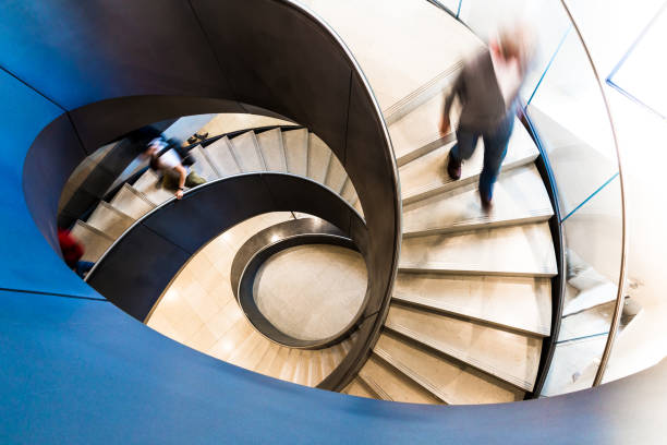 Motion Blur of People on Abstract Spiral Staircase Overhead view depicting blurred motion of people walking up and down a spiral staircase. The people are completely blurred, and the slow shutter speed makes it appear as though the people are moving fast. Image taken at City Hall in London, which is a publicly owned building that is accessible to the general public without any photographic restrictions. Room for copy space. moving down photos stock pictures, royalty-free photos & images