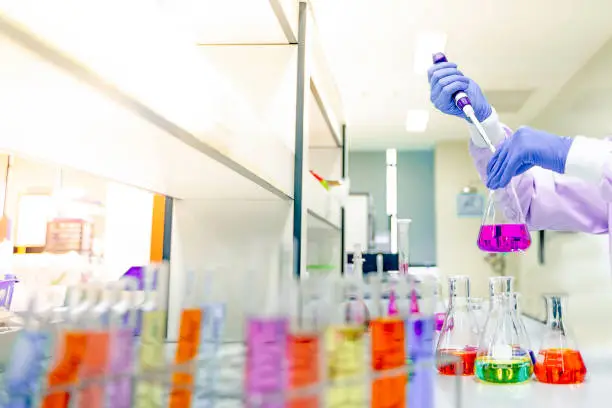Photo of scientist's hands put on the purple rubber gloves, experimenting with glass bottles containing various chemicals in the research and development concept in the science laboratory.shallow focus effect.