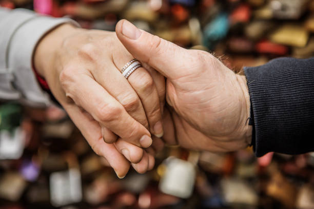 Groom holds his bride's hand against rose bush green leafs