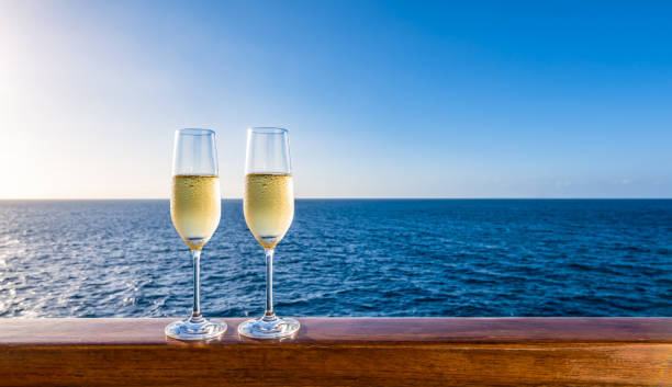 Two glasses of champagne on cruise vacation. Side view of two glasses of sparkling wine on a wooden railing of a cruise ship. Clear blue sky and sea background. Luxury alcoholic drinks on vacation. cruise ship photos stock pictures, royalty-free photos & images