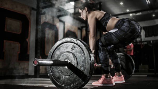 sport. donne muscolose che sollevano deadlift in palestra con bilanciere. interni drammatici con fumo. - gym barbell weights exercising foto e immagini stock