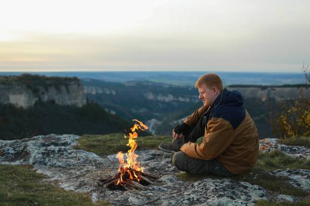 istock Man sits near campfire in mountains 1153368579