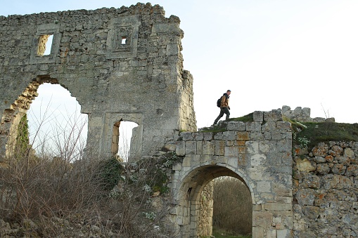 Redhead man in a brown-and-blue windbreaker rises to the ruins of a fortress in the cave city of Mangup-Kale in the Crimea. Travel, adventure, hiking and motivation concept.