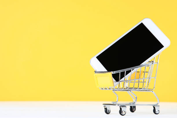 istock Small shopping cart with smartphone on yellow background 1153378607