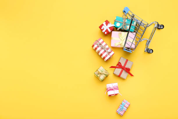 istock Small shopping cart with gift boxes on yellow background 1153378689