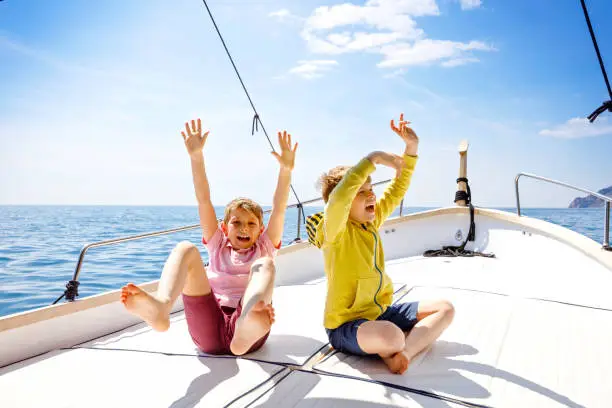 Photo of Two little kid boys, best friends enjoying sailing boat trip. Family vacations on ocean or sea on sunny day. Children smiling. Brothers, schoolchilden, siblings having fun on yacht.