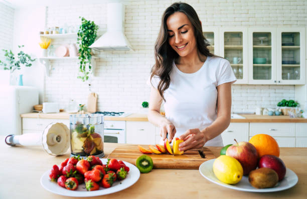 Beautiful woman making fruits smoothies with blender. Healthy eating lifestyle concept portrait of beautiful young woman preparing drink with bananas, strawberry and kiwi at home in kitchen. Make stock pictures, royalty-free photos & images