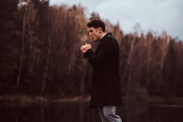 istock A handsome young man warms hands near a lake in the autumn forest. 1153382148