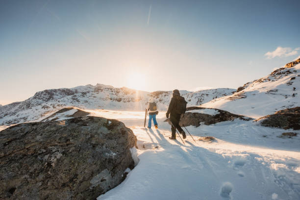 zwei bergsteiger wandern bei sonnenuntergang auf schneefeld zum gipfel - behind photographer men mountain climbing stock-fotos und bilder