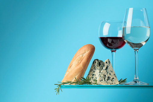 Blue cheese with baguette, wine and rosemary on a blue background. Copy space for your text.
