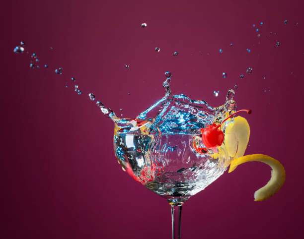 Ccktail in glass with splashes garnished with lemon and cherries.