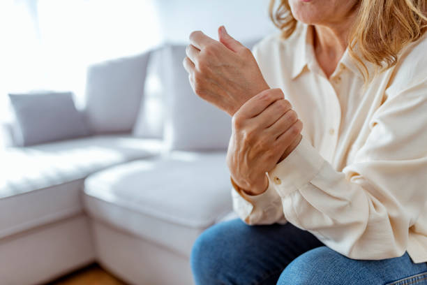 Senior woman rubbing her wrist and arm suffering from rheumatism Photo of Elderly lady is enduring strong ache while sitting on the sofa during the day. Senior Woman At Home Suffering With Arthritis. Upset stressed mature middle-aged woman feeling pain ache. chronic illness photos stock pictures, royalty-free photos & images
