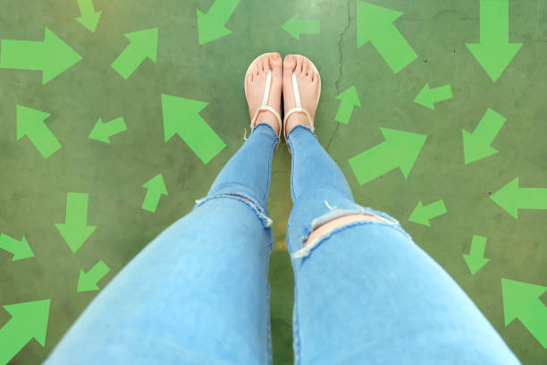 diferentes flechas de dirección hacia el futuro. selfie sobre mujer de pie con opciones de línea de flecha verde. zapatos mujer (calzado) y flechas en street road en el fondo de la ciudad. - choice teenager footpath arrow sign fotografías e imágenes de stock