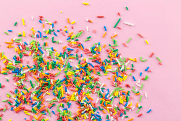 istock Sprinkles on pink background - Many multi-colored sprinkles on pink - top view 1153400428