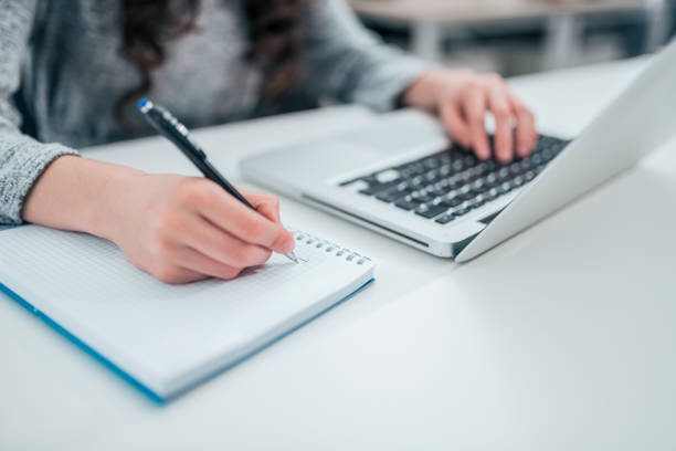 istock Close up of woman's hands writing in spiral notepad and using laptop. 1153406019