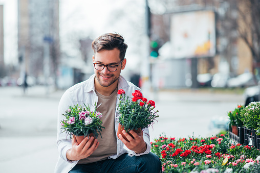 Smiling young man holding two potted plants outdoors, buying flowers.
