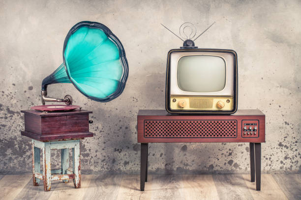 Vintage antique mint blue gramophone phonograph turntable on aged stool and old television from 50s on wooden TV stand front grunge textured loft concrete wall background. Retro style filtered photo