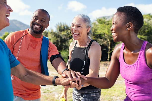 Mature people stacking hands after workout Laughing senior and multiethnic sports people putting hands together at park. Happy group of men and women smiling and stacking hands outdoor. Multiethnic sweaty team cheering after intense training. 30s 40s activity adult stock pictures, royalty-free photos & images