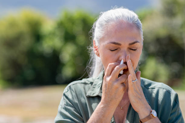 Woman using nasal spray for allergy Senior woman having flu using nasal spray to help herself. Woman using a nasal spray at park for allergy. Ill mature woman with grey hair inhaling medicine against allergy. nose flower stock pictures, royalty-free photos & images