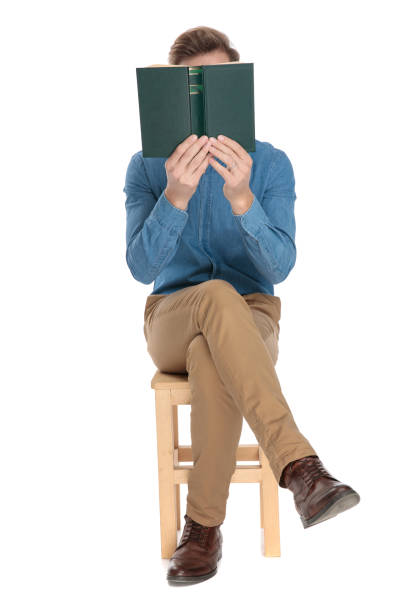 giovane ragazzo in possesso di un libro davanti al suo viso - casual smart casual sex symbol sensuality foto e immagini stock