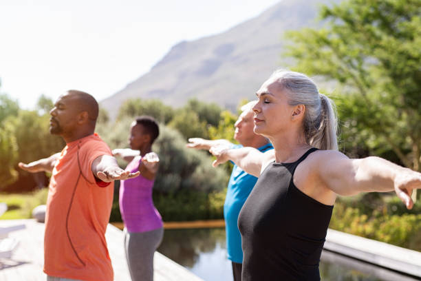 Mature group of people doing breathing exercise Group of senior people with closed eyes stretching arms outdoor. Happy mature people doing breathing exercise near pool. Yoga class with women and men doing breath exercise with outstretched arms. Balance and meditation concept. yoga class photos stock pictures, royalty-free photos & images