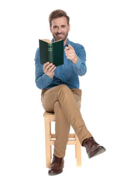 istock Cheerful young man holding a book and pointing 1153409400