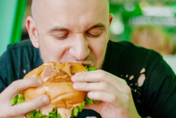 istock Man in a restaurant eating a hamburger, he is hungry and having a good bite. selective focus 1153409422