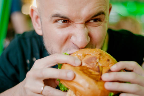 istock Man in a restaurant eating a hamburger, he is hungry and having a good bite. selective focus 1153409514