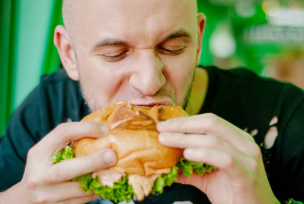istock Man in a restaurant eating a hamburger, he is hungry and having a good bite. selective focus 1153409523