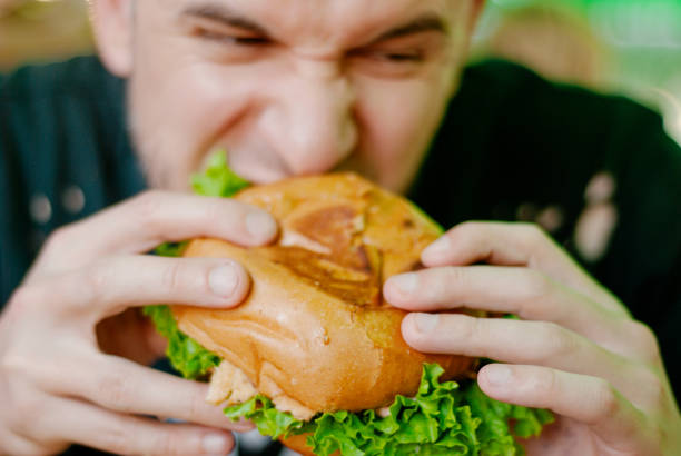 istock Man in a restaurant eating a hamburger, he is hungry and having a good bite. selective focus 1153409529